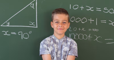 Portrait of happy caucasian boy standing at chalkboard in maths lesson classroom holding schoolbook. childhood and education at elementary school.